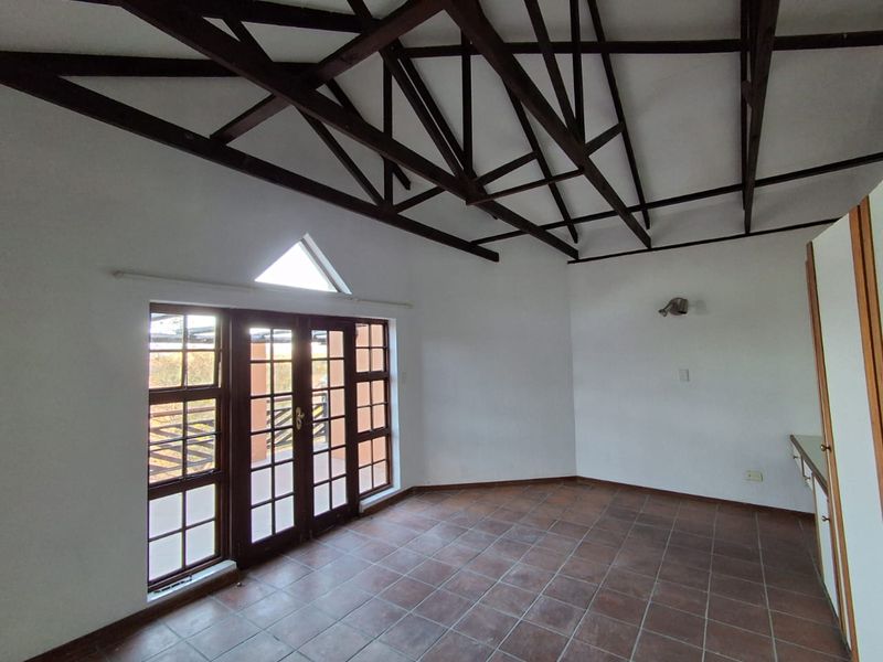 Spacious living area featuring high vaulted ceilings with exposed timber trusses, tiled flooring, and large french doors leading to an outdoor space.