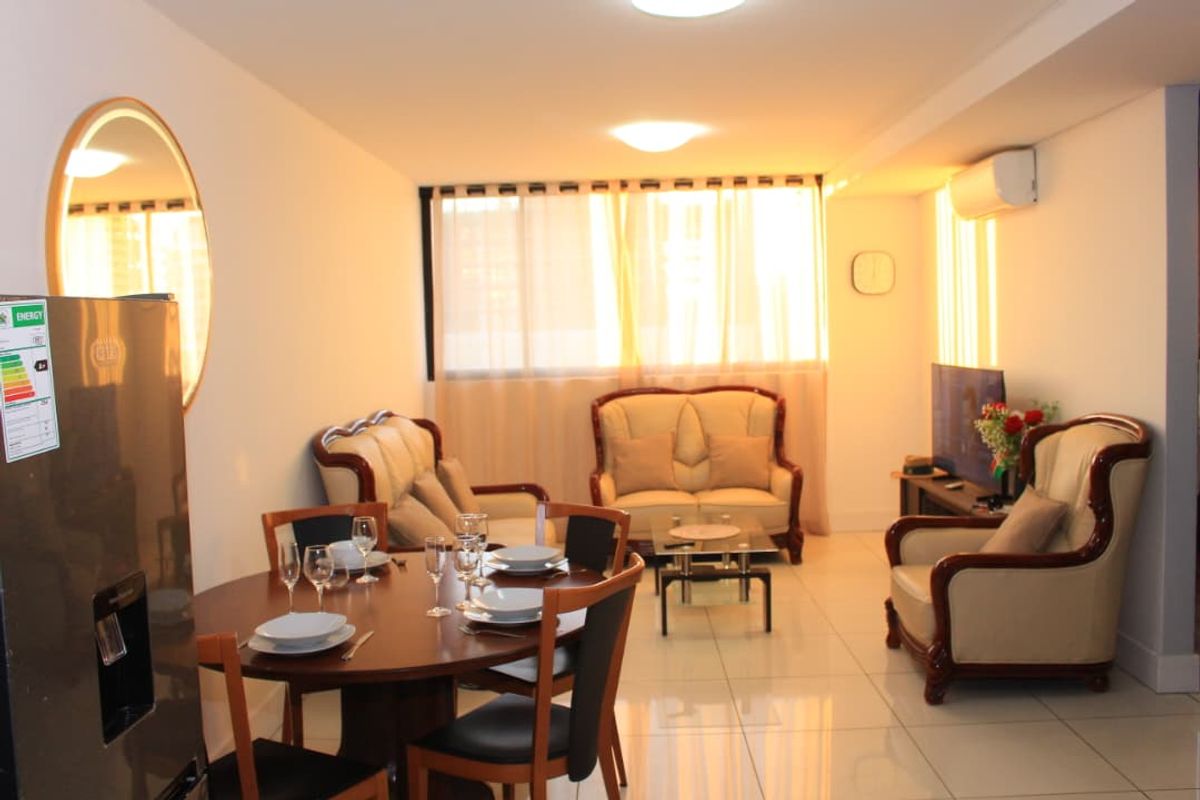 An open-plan living and dining area featuring polished tiled flooring, recessed ceiling lighting, and a wall-mounted air conditioning unit.