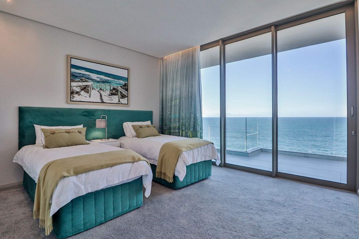 Modern bedroom featuring floor-to-ceiling sliding glass doors that open to a balcony with expansive ocean views and a glass balustrade.