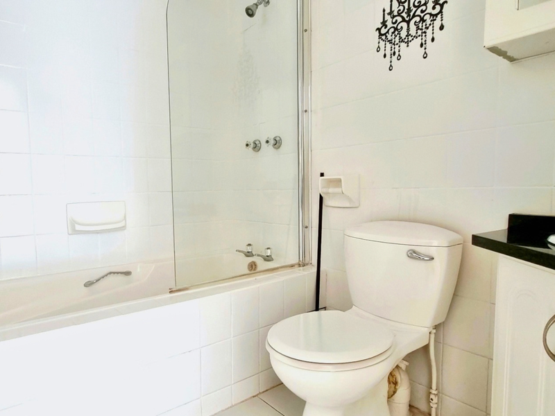 A functional bathroom featuring a bathtub with a glass shower screen, a white toilet, and a vanity cabinet with a black granite countertop.