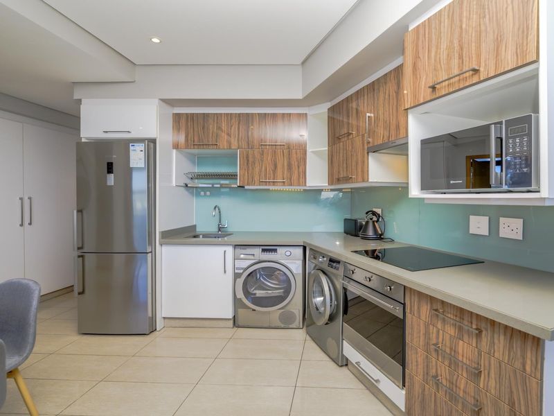 Modern kitchen featuring wood-grain cabinetry, stone countertops, glass splashback, and integrated stainless steel appliances including an oven, hob, and microwave.