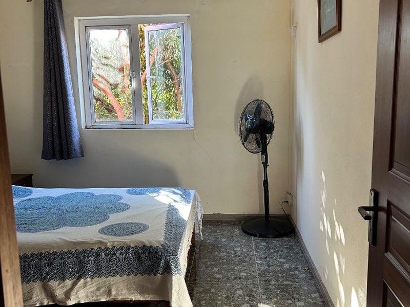 A bedroom featuring tiled flooring, a casement window, and a pendant light fixture, currently showing signs of wear on the wall surfaces.