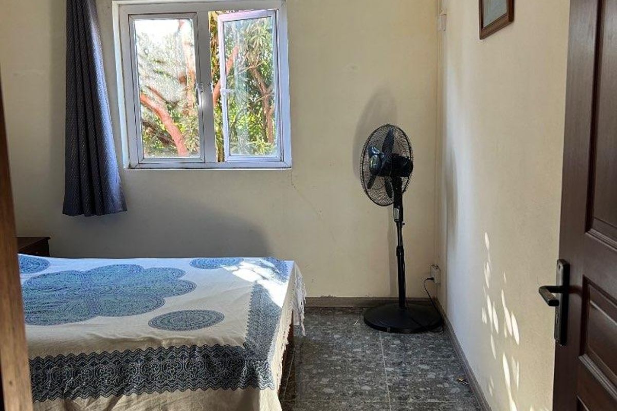 A bedroom featuring tiled flooring, a casement window, and a pendant light fixture, currently showing signs of wear on the wall surfaces.