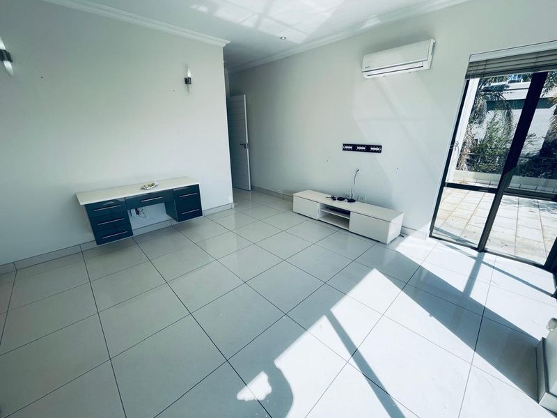 A bright, open-plan living area featuring large format floor tiles, a wall-mounted air conditioning unit, and direct access to an outdoor patio.