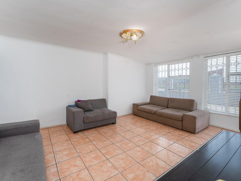 A living room featuring ceramic floor tiles, security bars on windows, and a central ceiling light fixture.
