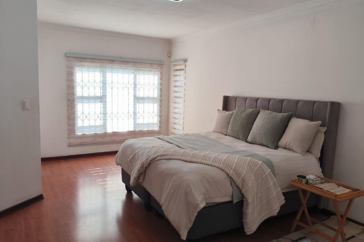 A well-maintained bedroom featuring laminate flooring, secure window treatments, and a modern ceiling light fixture.