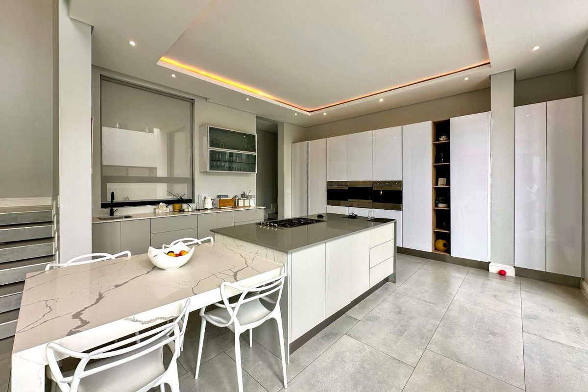 Modern kitchen featuring a large central island, integrated appliances, sleek cabinetry, stone countertops, and sophisticated recessed ceiling lighting.
