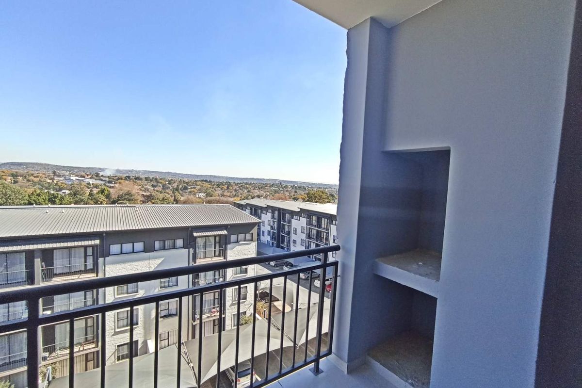 A covered balcony featuring a built-in braai, metal balustrade, and expansive views over the surrounding residential complex and landscape.