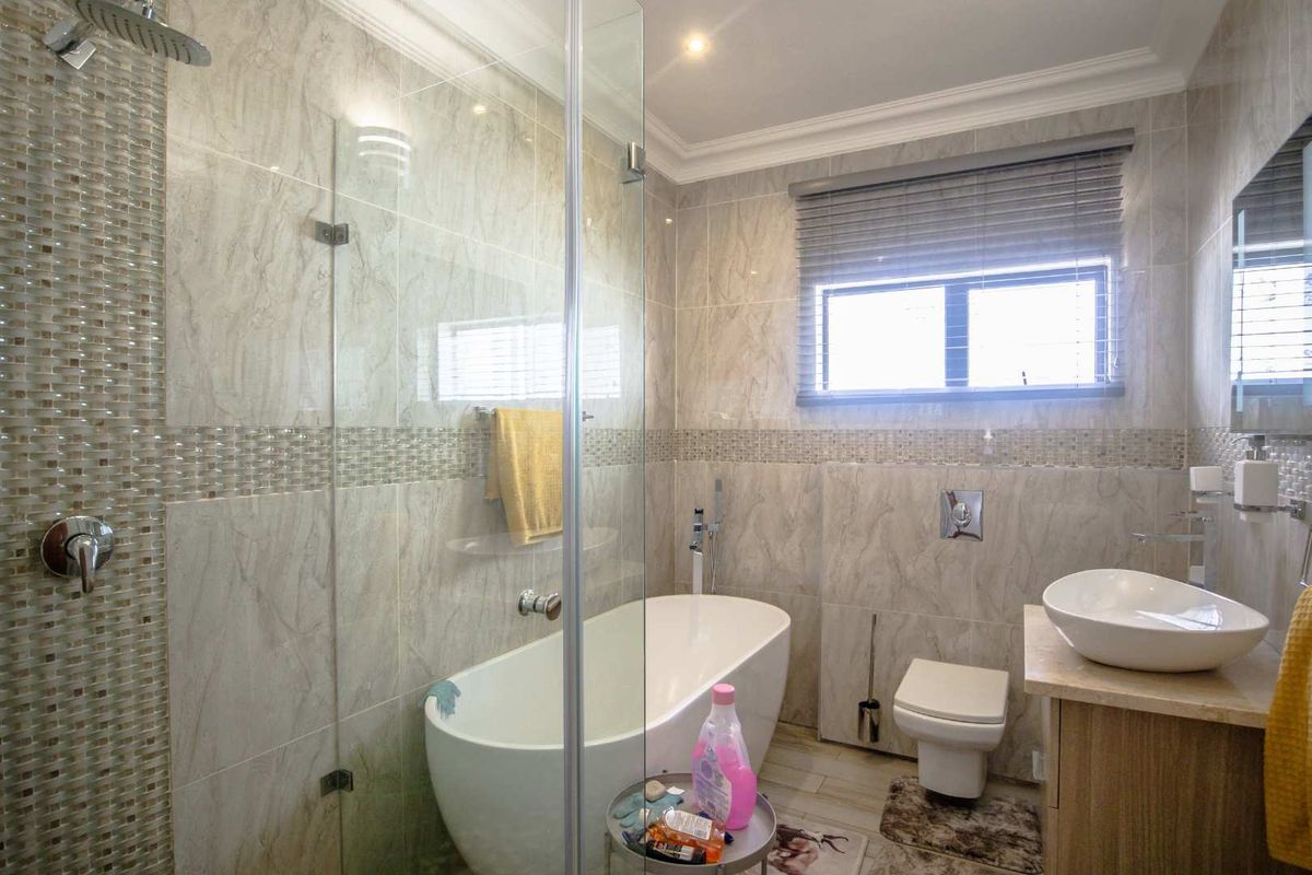 Modern bathroom featuring a freestanding bathtub, glass-enclosed shower, wall-mounted toilet, and a vessel sink vanity with marble-look wall tiling.