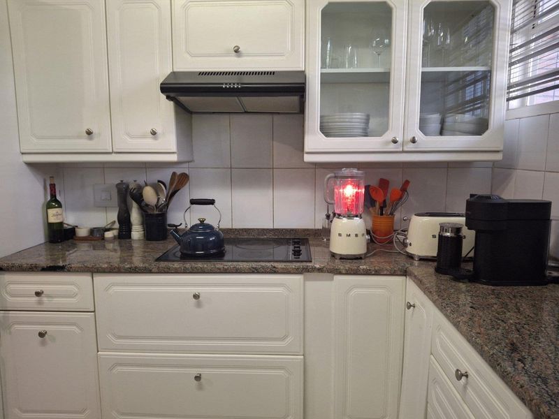 A functional kitchen featuring white cabinetry, granite countertops, a tiled backsplash, and a built-in electric hob with an extractor fan.