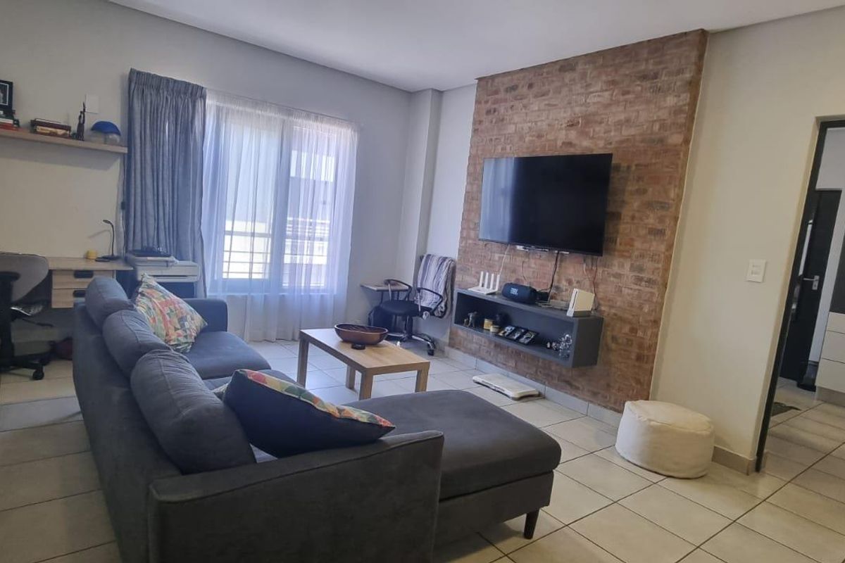A comfortable living room featuring an exposed brick accent wall, built-in media shelving, and a dedicated workspace area with tiled flooring throughout.
