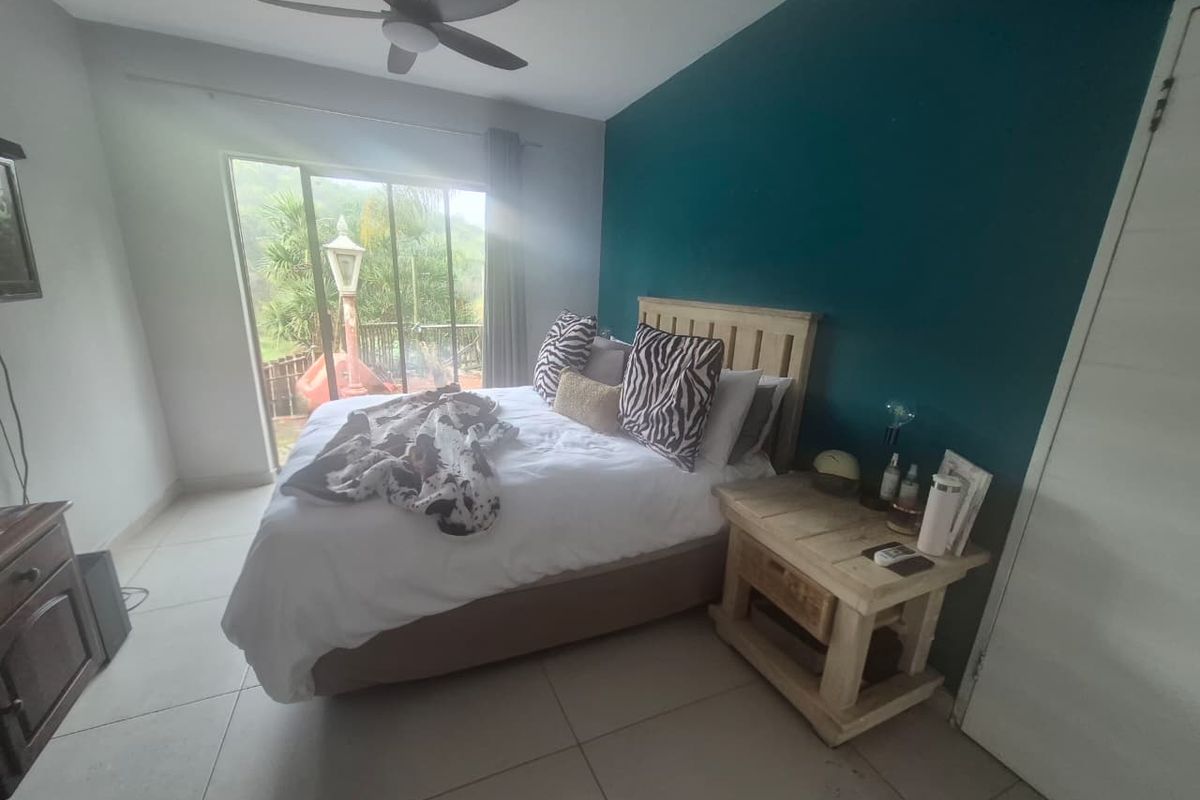 A bedroom featuring tiled flooring, a ceiling fan, and a sliding glass door providing access to the outdoors, complemented by a teal accent wall.