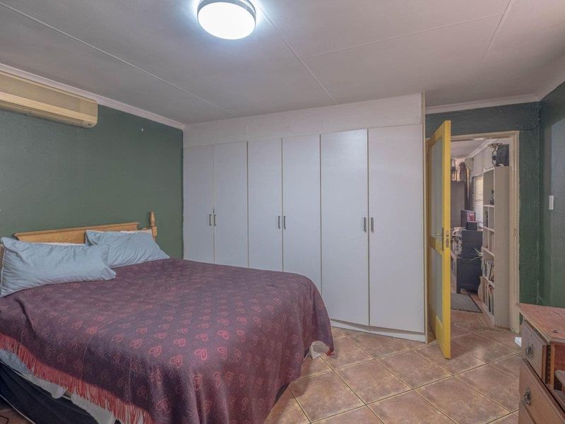 A bedroom featuring built-in cupboards, tiled flooring, and a wall-mounted air conditioning unit.