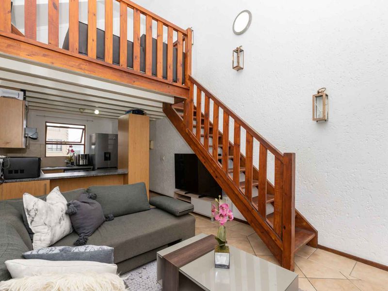 Open-plan living area featuring a wooden staircase leading to a mezzanine level, integrated kitchen cabinetry, and tiled flooring throughout.