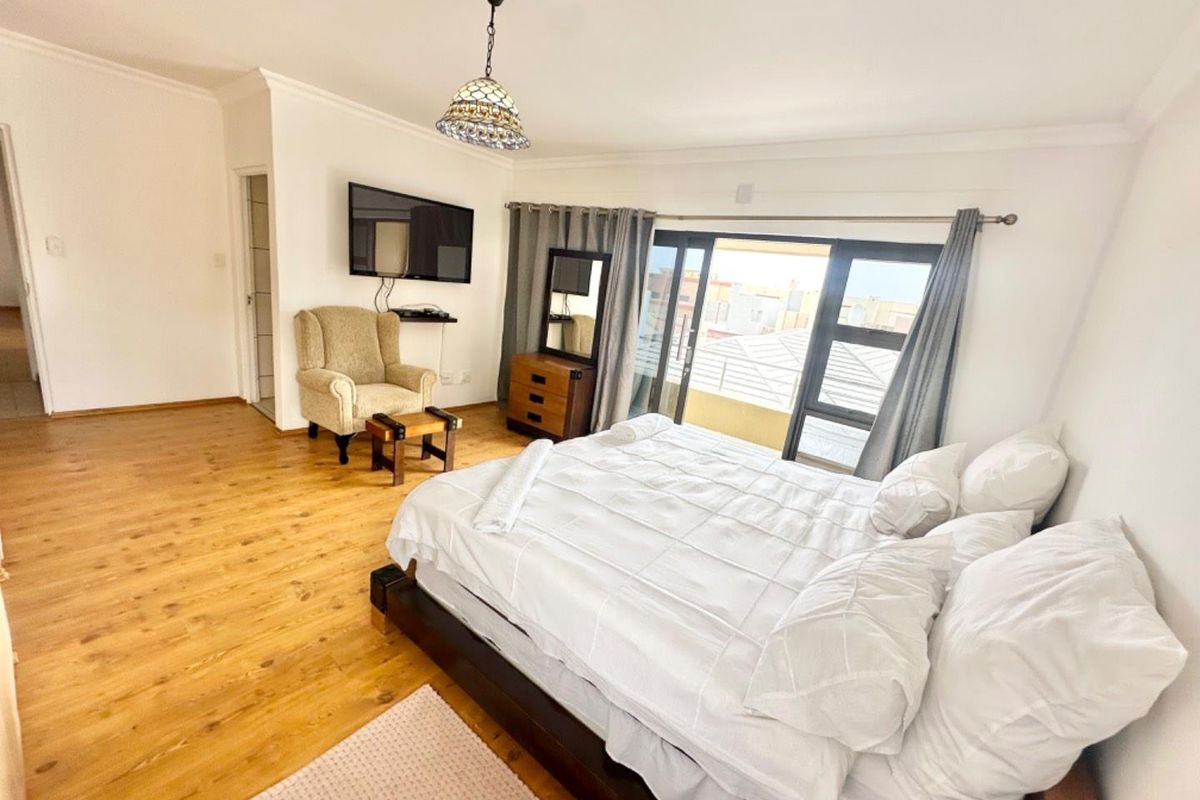 Spacious bedroom featuring light wood-look flooring, large sliding glass doors leading to a balcony, and neutral wall finishes.