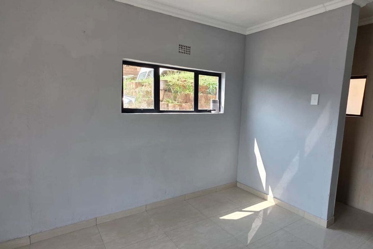 An empty bedroom featuring tiled flooring, a pedestal basin, and an aluminium window frame, awaiting personal touches to complete the space.
