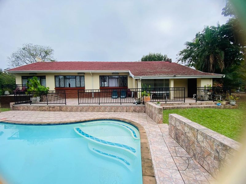 Rear view of the house featuring a swimming pool, tiled patio area, and secure metal fencing, set against a landscaped garden.