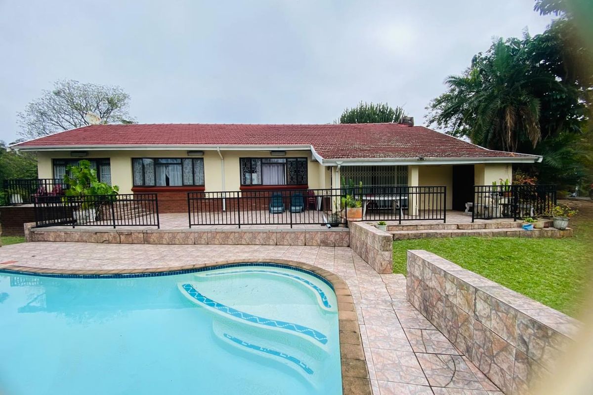 Rear view of the house featuring a swimming pool, tiled patio area, and secure metal fencing, set against a landscaped garden.