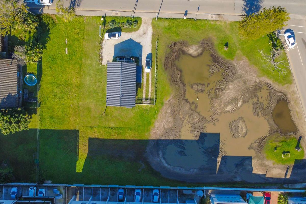 Aerial view of a vacant residential plot featuring a driveway, fencing, and significant areas of waterlogged, uneven ground.