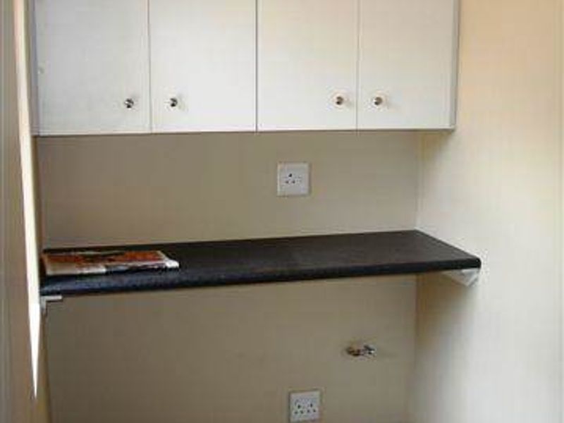 A functional laundry or utility nook featuring wall-mounted storage cabinets, a dark laminate work surface, and dedicated plumbing and electrical connections.