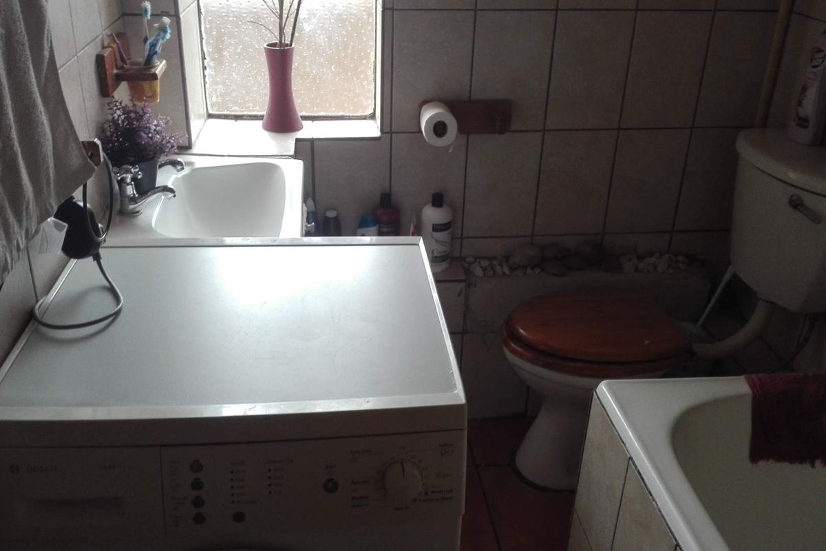 A compact bathroom featuring a bathtub, toilet, and washbasin with tiled finishes. The space is dated and would benefit from a modern renovation.