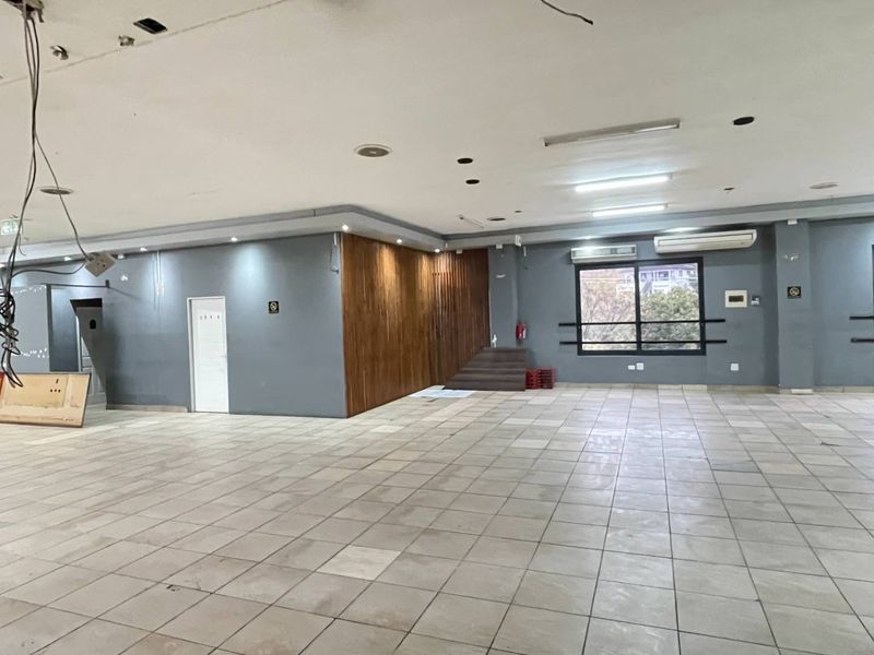 A large, open-plan industrial space featuring tiled flooring, timber wall accents, and exposed electrical wiring, suitable for a variety of commercial or office uses.