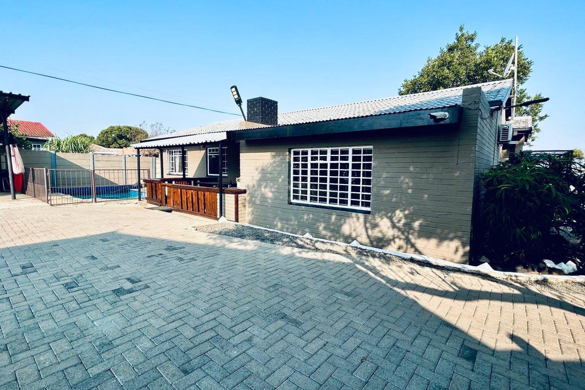 Rear view of the property featuring a paved courtyard, a covered patio area, and a swimming pool with perimeter fencing.