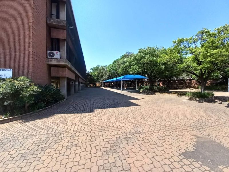 Exterior view of the office building featuring a paved parking area with shaded carports and mature trees.