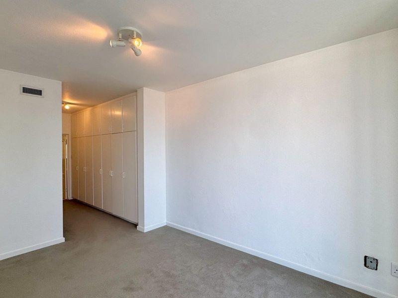 A spacious, empty bedroom featuring neutral carpeting, extensive built-in cupboard storage, and a clean, minimalist aesthetic ready for personalization.