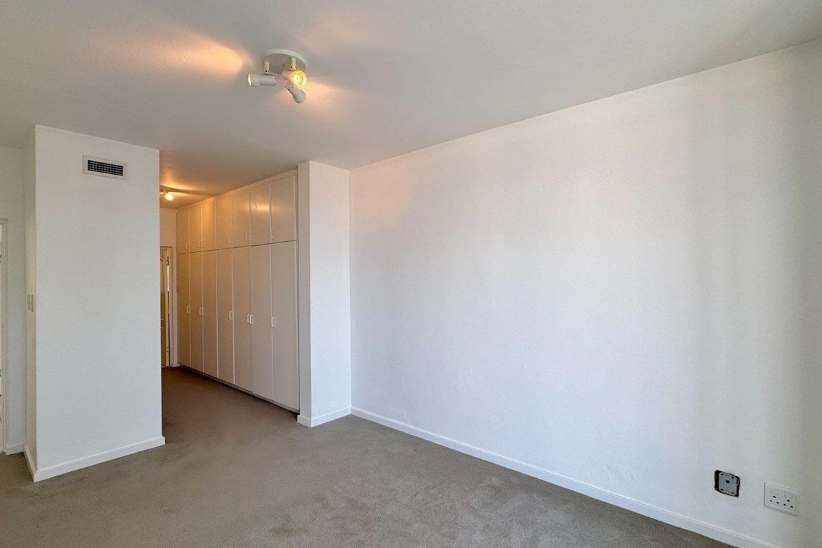 A spacious, empty bedroom featuring neutral carpeting, extensive built-in cupboard storage, and a clean, minimalist aesthetic ready for personalization.