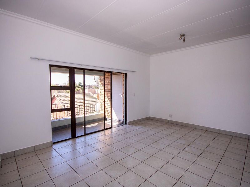A bright, empty living room featuring neutral tiled flooring and a sliding glass door that opens onto a private balcony.