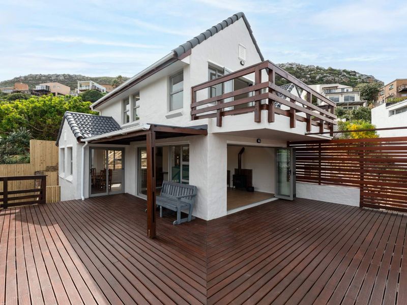 Spacious rear timber deck featuring a covered patio area, upper-level balcony with timber balustrade, and bi-fold doors leading into the home.