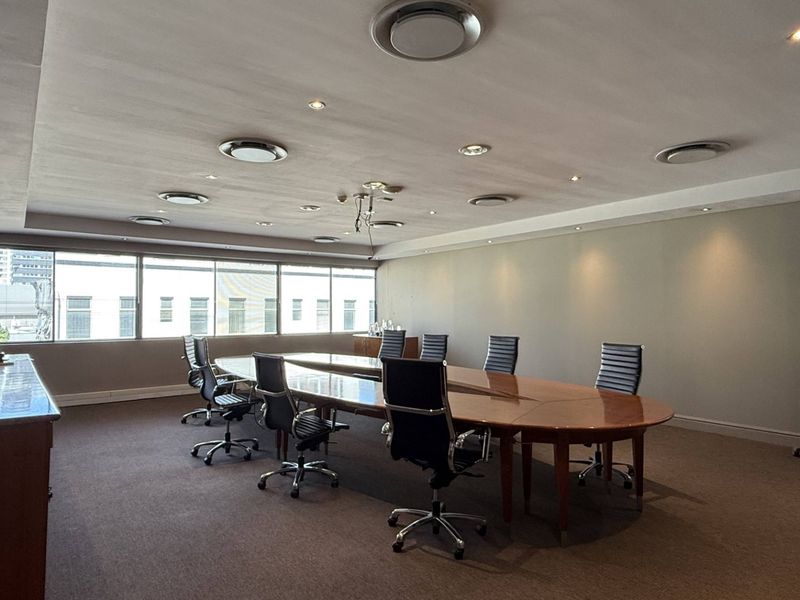A professional boardroom featuring large windows, recessed ceiling lighting, and built-in cabinetry, providing a functional and well-lit workspace.
