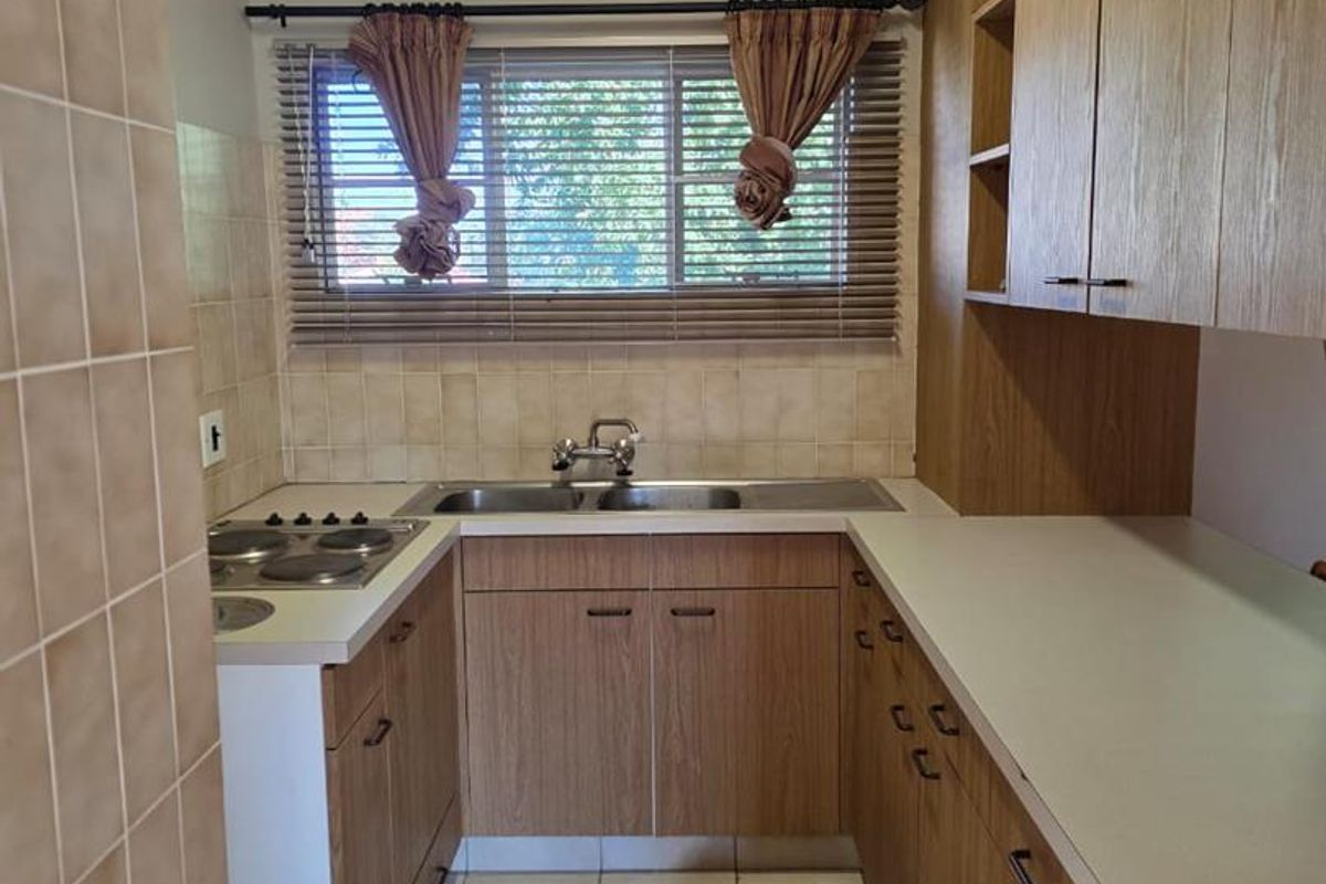 A functional kitchen featuring wood-look cabinetry, tiled splashbacks, a built-in hob, and a double-basin sink under a window.