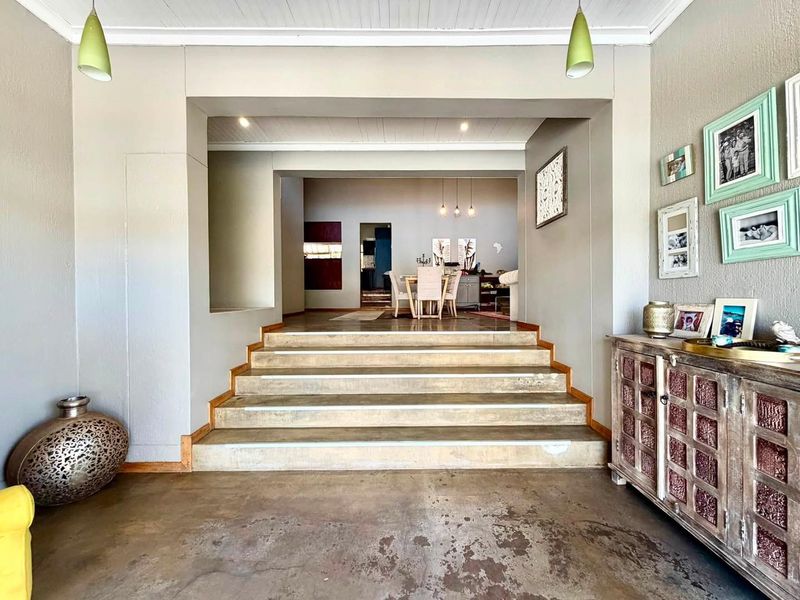 Spacious living area featuring concrete flooring and a set of stairs leading to an elevated dining space with recessed and pendant lighting.