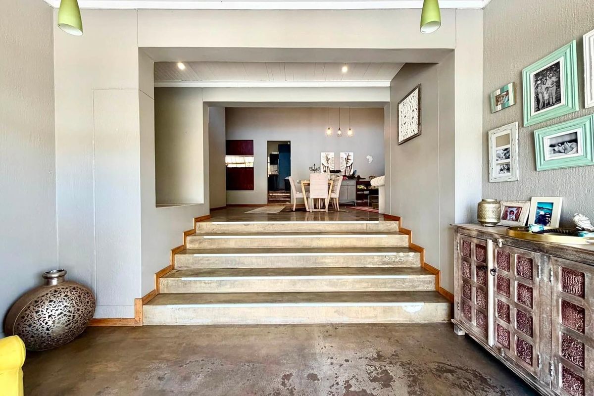 Spacious living area featuring concrete flooring and a set of stairs leading to an elevated dining space with recessed and pendant lighting.