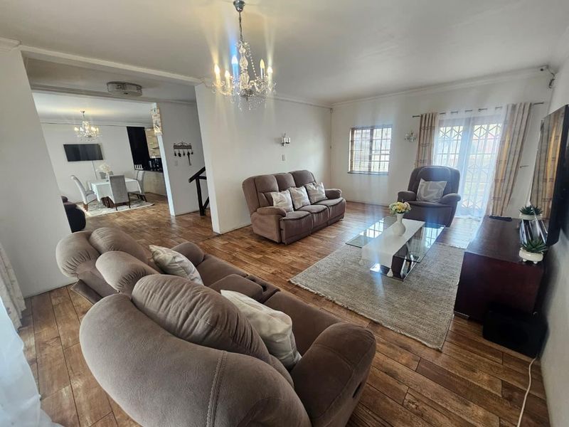 Spacious open-plan living area featuring wood-look tile flooring, elegant chandelier lighting, and direct access to the exterior through a secure sliding glass door.