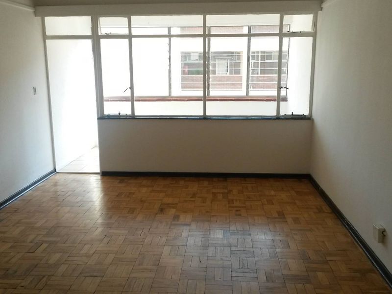 An empty living room featuring original parquet flooring and large metal-framed windows that provide ample natural light.