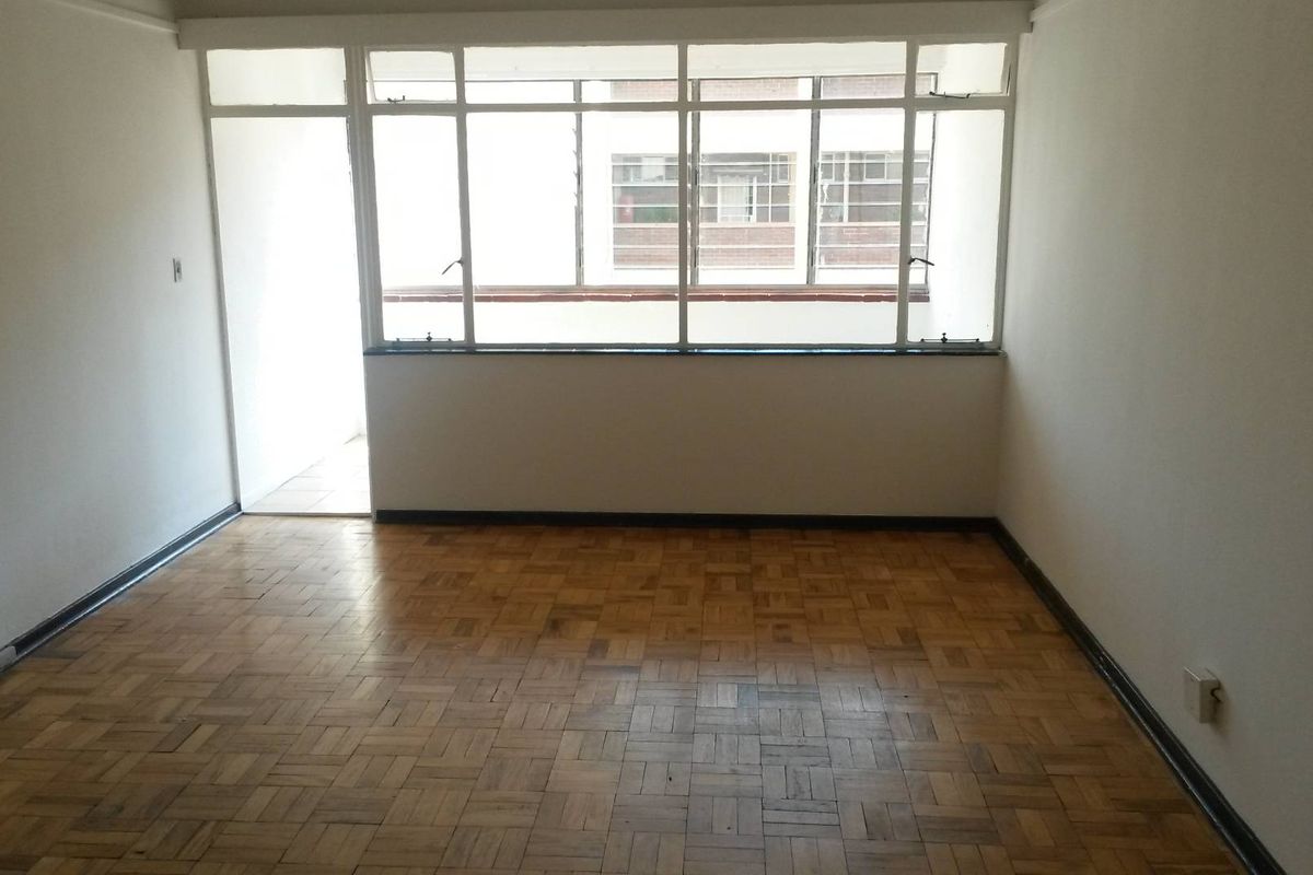 An empty living room featuring original parquet flooring and large metal-framed windows that provide ample natural light.