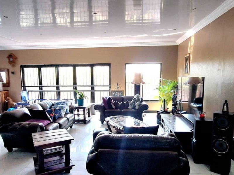 Spacious open-plan living and dining area featuring large glass sliding doors with security bars, tiled flooring, and a high-gloss ceiling finish.