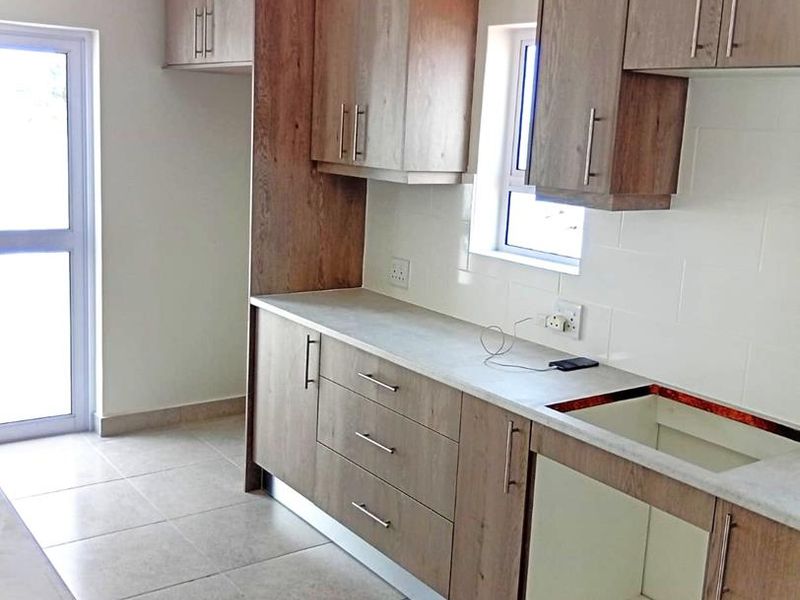 A modern kitchen featuring wood-look cabinetry, tiled flooring, and a tiled backsplash, currently awaiting the installation of a sink and stove.