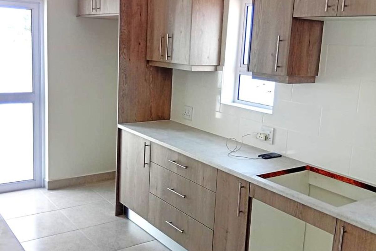 A modern kitchen featuring wood-look cabinetry, tiled flooring, and a tiled backsplash, currently awaiting the installation of a sink and stove.