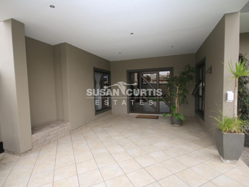 A covered patio area featuring tiled flooring, recessed downlighting, and a built-in brick bench, providing a functional outdoor entertainment space.