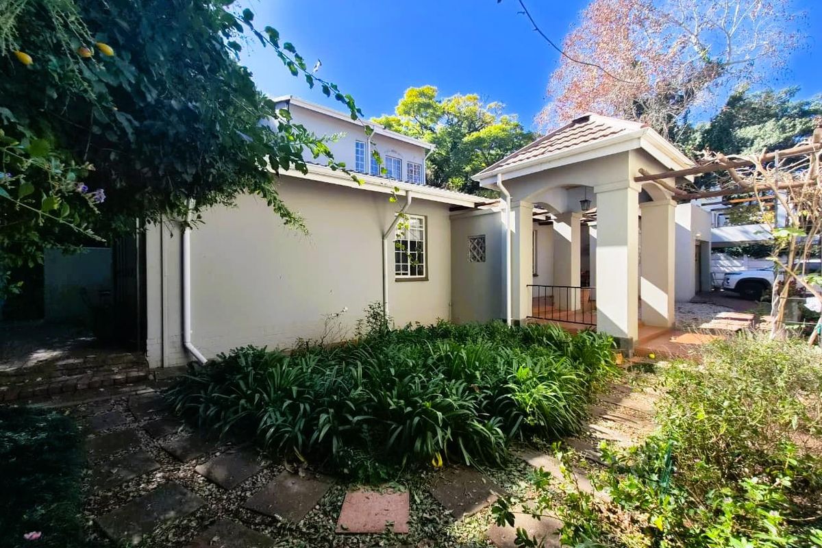 Rear view of the property featuring a covered patio area, paved garden pathways, and established landscaping.