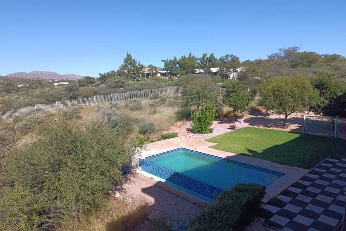 Outdoor pool area featuring a tiled swimming pool, adjacent lawn, and paved patio space set within a landscaped garden with perimeter fencing.