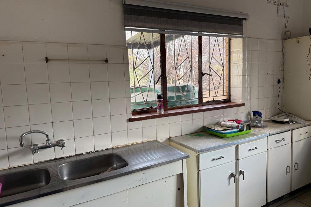 A dated kitchen featuring a stainless steel double sink, tiled splashbacks, and original cabinetry, offering significant potential for a modern renovation.