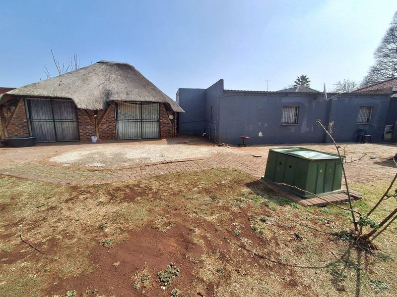 Rear exterior view featuring a thatched roof structure, brick paved patio area, and a large garden space requiring landscaping.