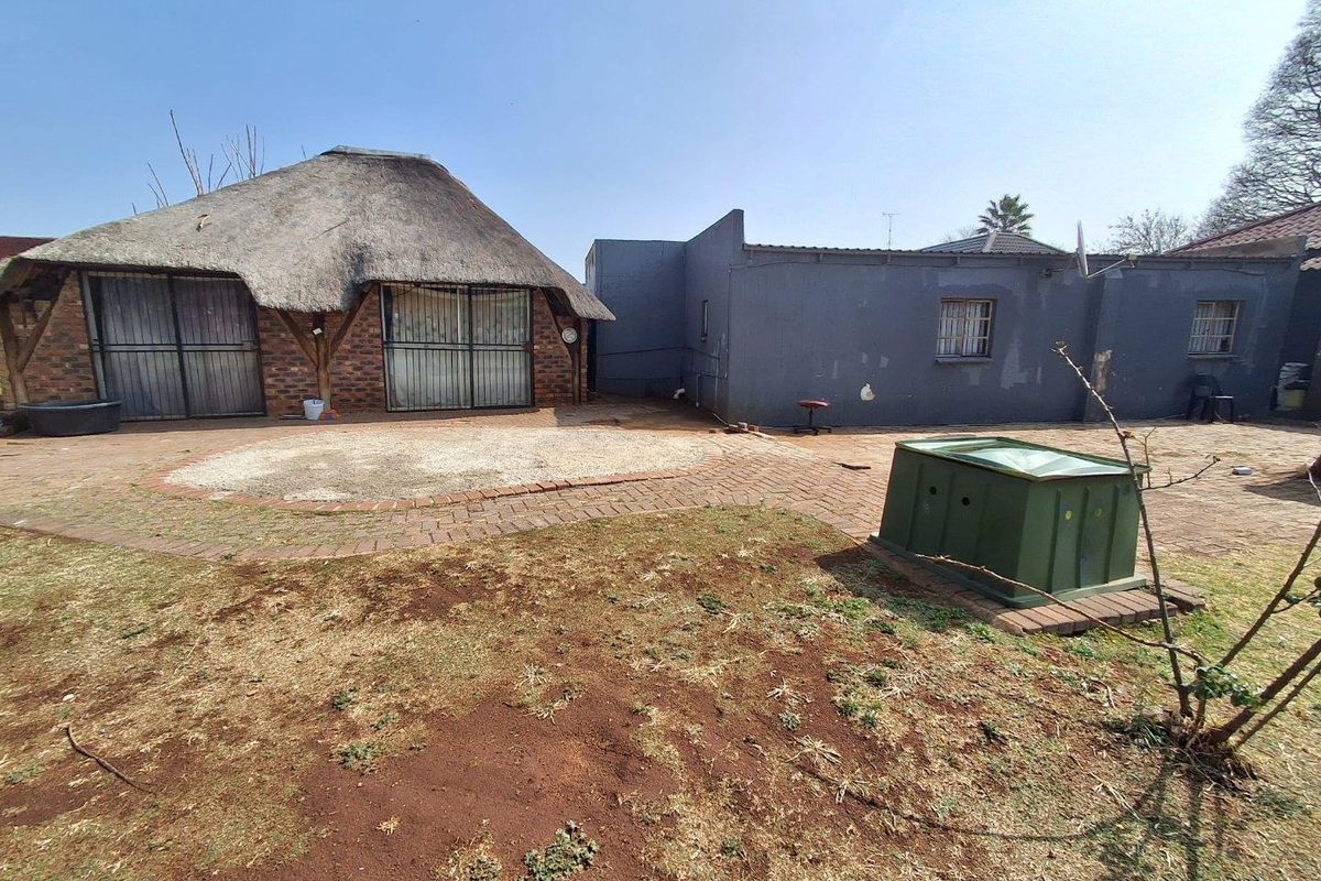 Rear exterior view featuring a thatched roof structure, brick paved patio area, and a large garden space requiring landscaping.
