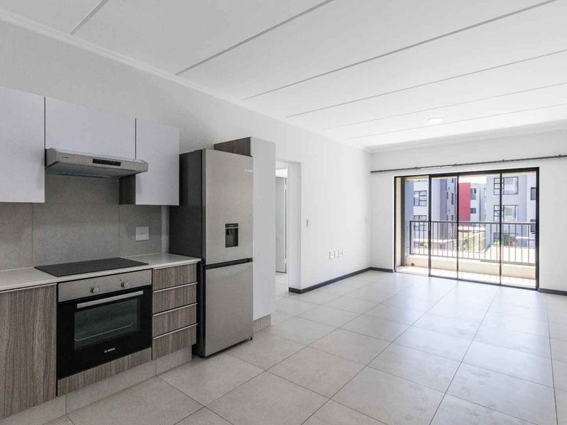 Modern open-plan kitchen and living area featuring sleek cabinetry, built-in appliances, and large sliding doors leading to a private balcony.