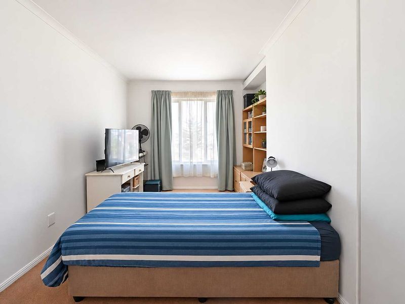 A functional bedroom featuring neutral walls, carpeted flooring, and built-in shelving, providing a comfortable and practical living space.